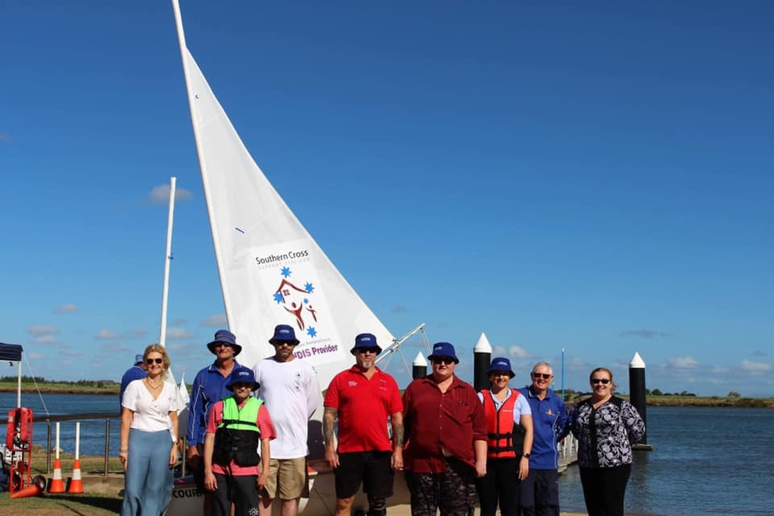 Gruppfoto av medlemmar vid en segelbåt med 'Southern Cross'-märkning.