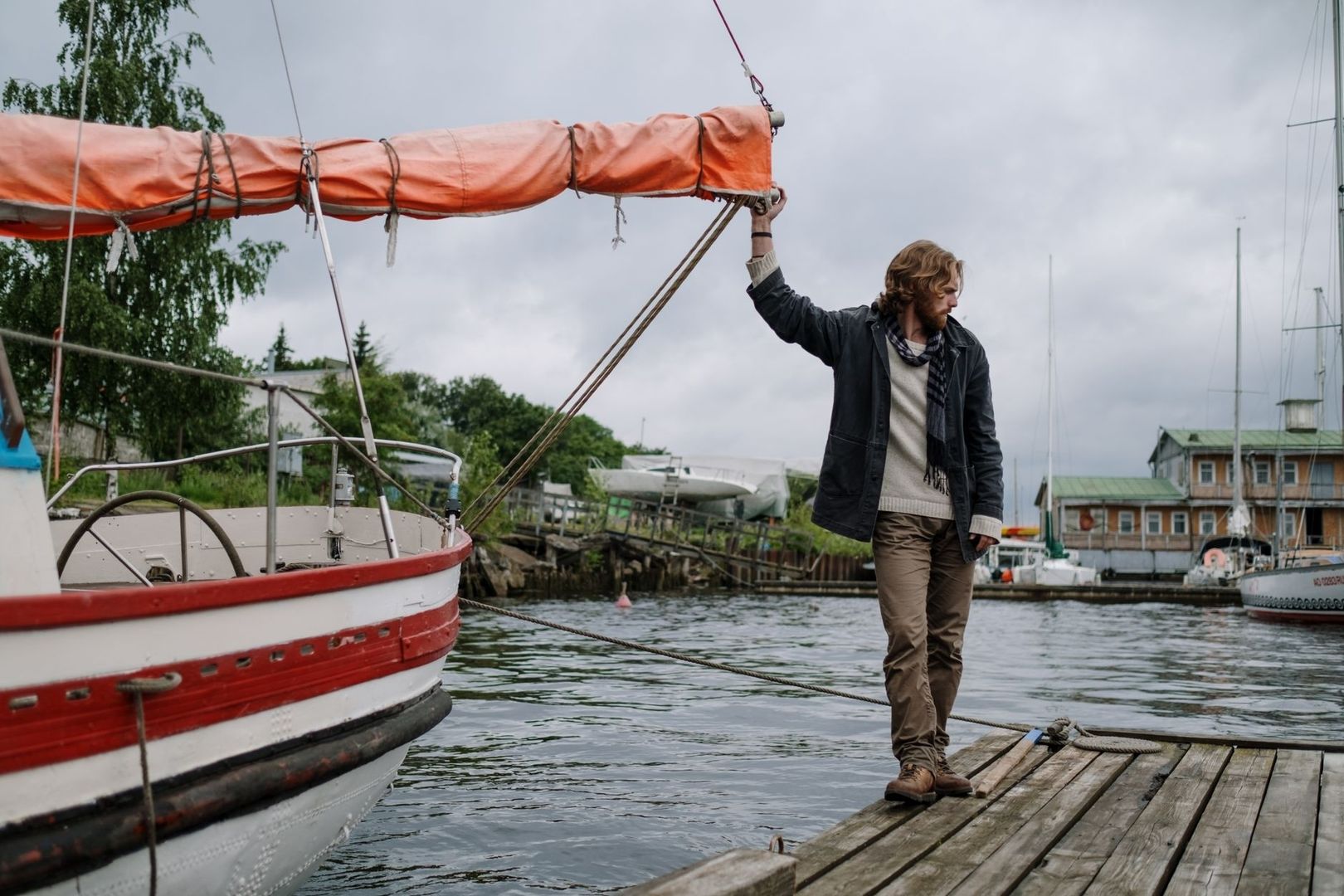 Man håller i en segelbåts bom vid en träbrygga i hamnen